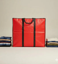 Red tote bag with black handles next to folded clothes on a beige background
